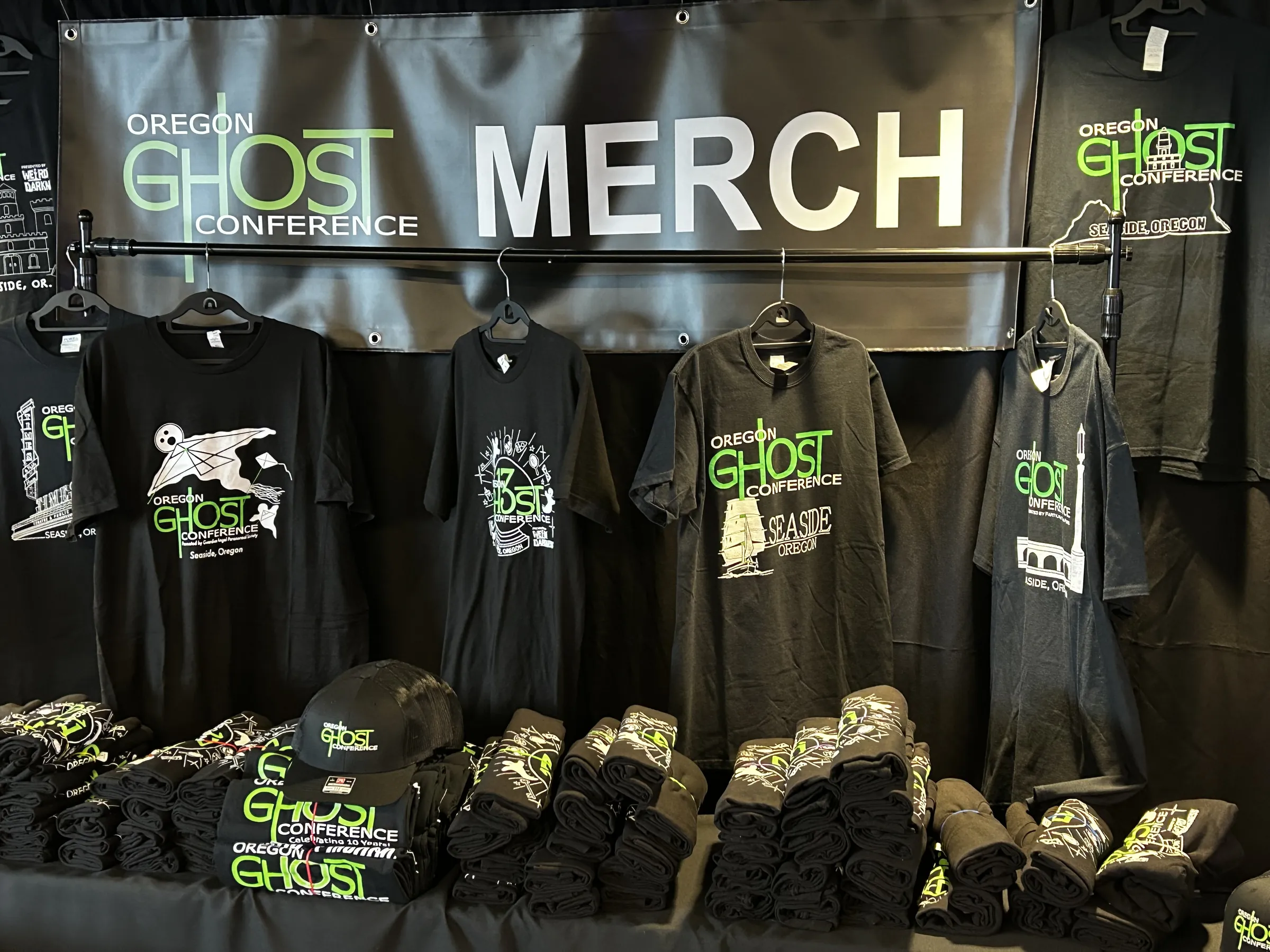The official merch wall, t-shirts and hats in ghost green under the Oregon Ghost Conference banner