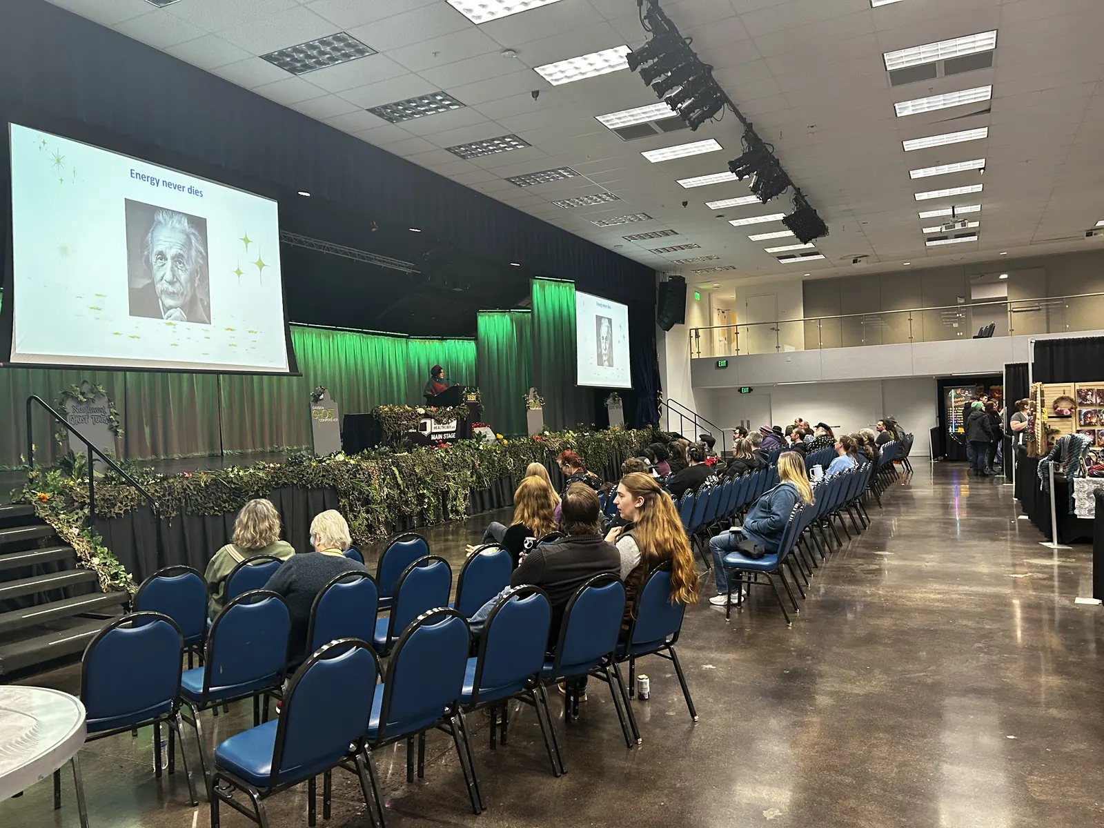 The main hall mid-presentation, screens glowing over the audience